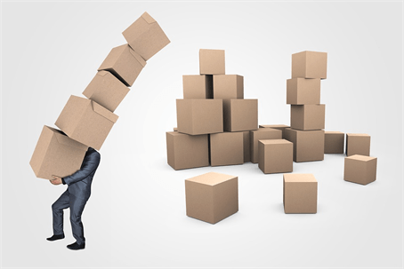 A man in a suit struggles to carry an unsteady stack of boxes on his head.