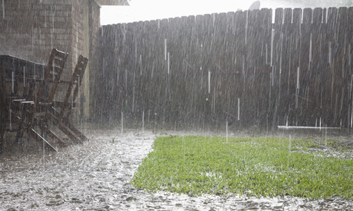 A downpour soaks a backyard with wooden furniture and fencing