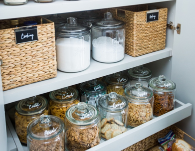 Neatly organized pantry shelves show labelled jars and baskets with food items.
