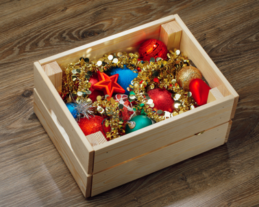 A wooden crate is filled with colorful Christmas decorations.