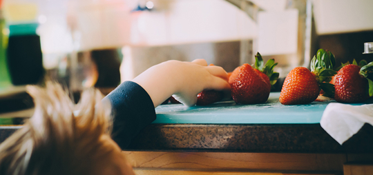 A kid is reaching for strawberries