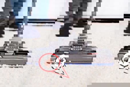 A person vacuums a carpet with a tick